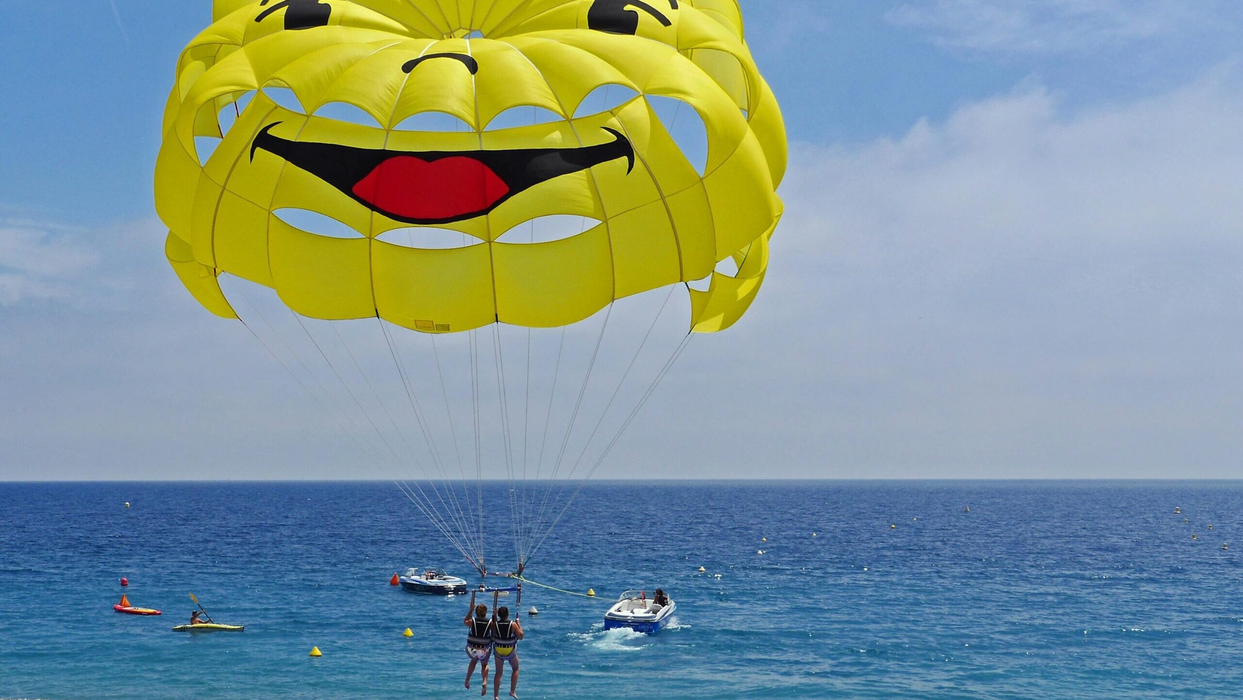 Parasailing over vibrant blue waters with a smiley face parachute, capturing summer fun and adventure.