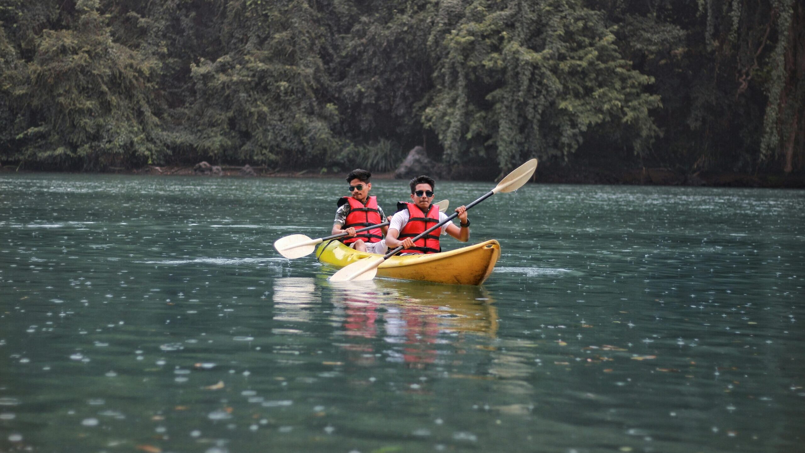 Two people enjoying kayaking on Kali River surrounded by lush greenery in Dandeli, India.