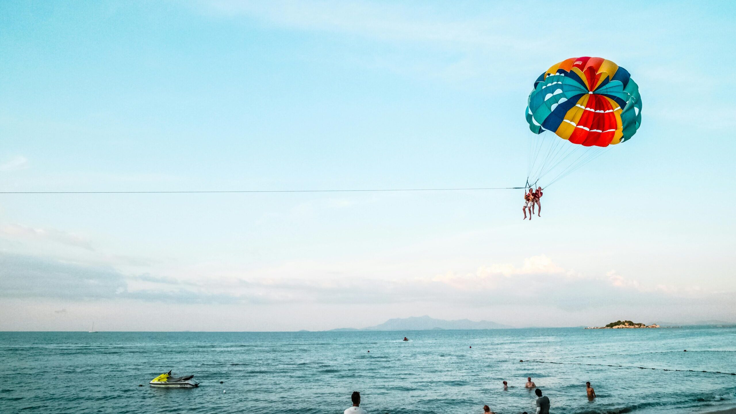 Exciting parasailing experience over the ocean with a vibrant parachute and scenic beach view.