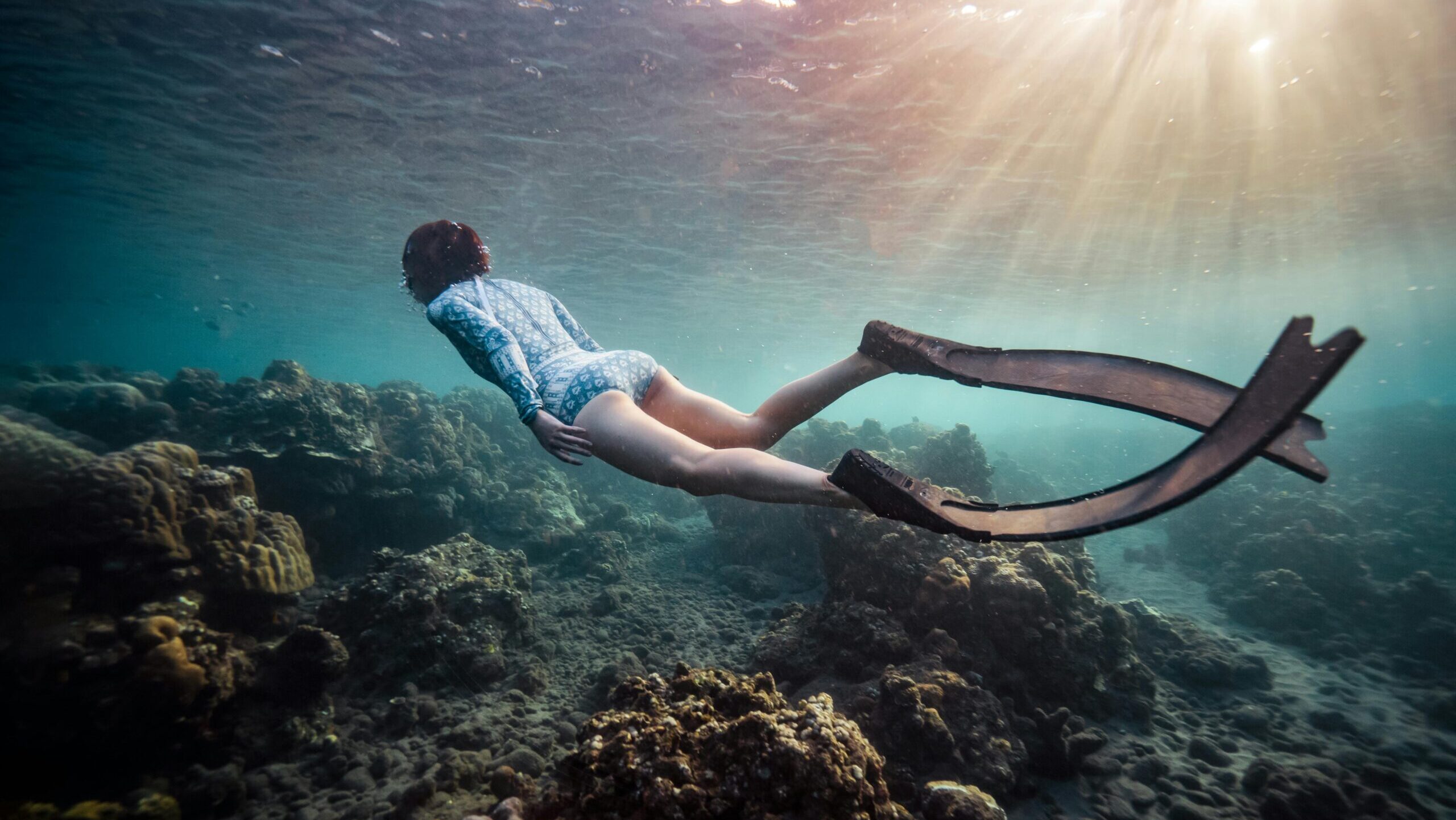 A freediver swims over vibrant coral reefs, soaking in underwater beauty and tranquility.