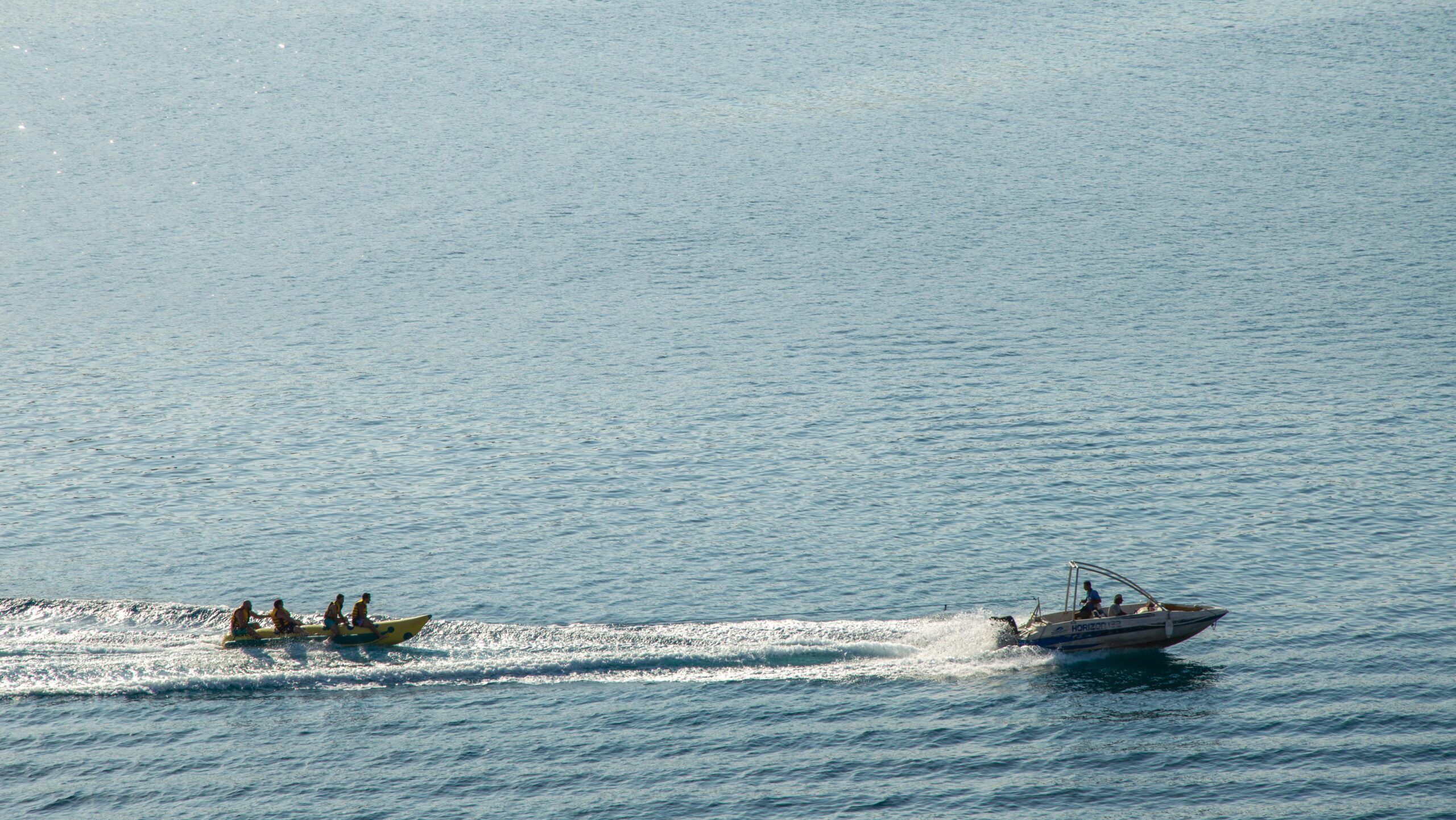 Motorboat towing a banana boat with people enjoying a sunny day at the open sea.