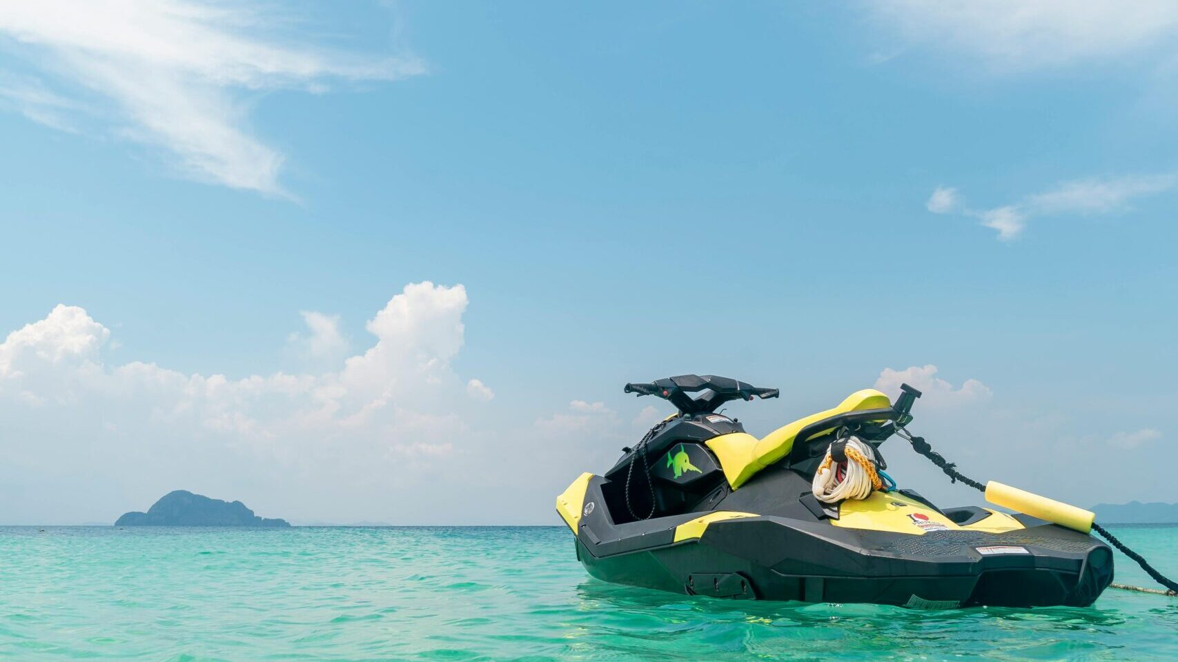 Jet ski floats on clear turquoise waters with a scenic island backdrop and blue skies.
