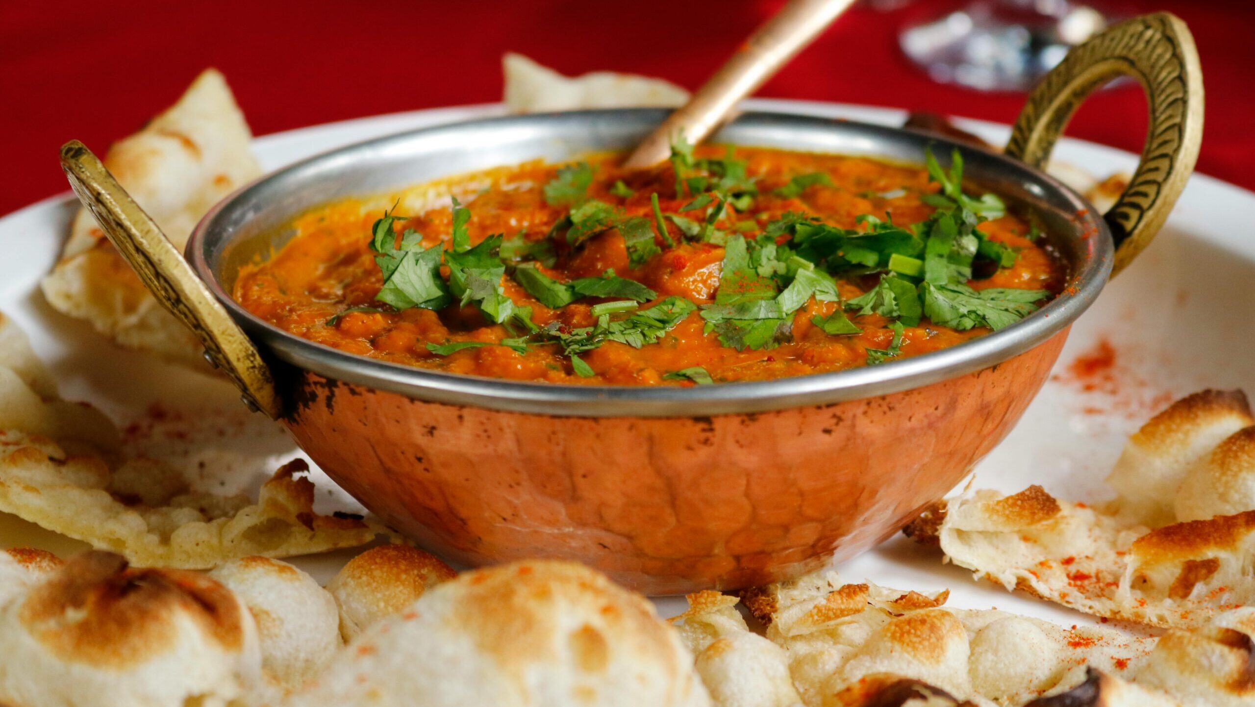 Delicious Indian curry garnished with cilantro served with naan in a copper dish.