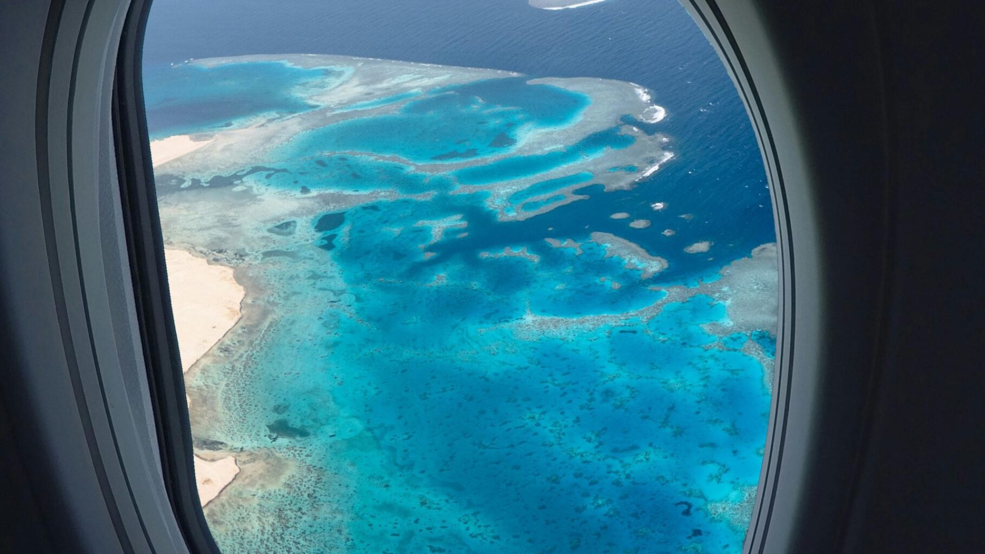 pexels-photo-1260991-1260991 Breathtaking aerial view of ocean reefs through an airplane window, showcasing vibrant blues from above.